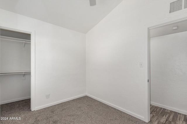 unfurnished bedroom with ceiling fan, a closet, lofted ceiling, and dark colored carpet