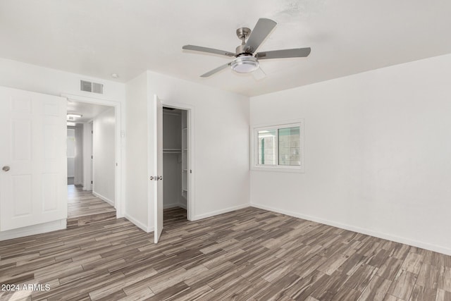 unfurnished bedroom featuring a walk in closet, a closet, ceiling fan, and dark wood-type flooring