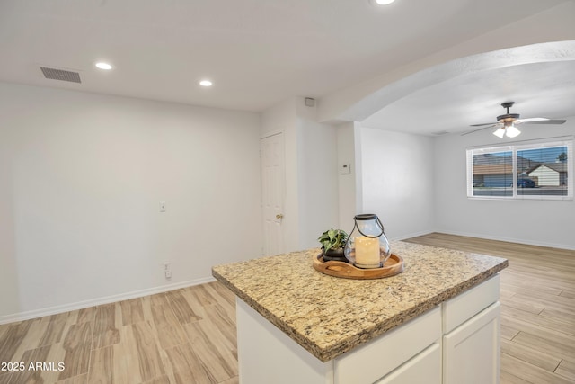 kitchen with a kitchen island, light stone counters, white cabinets, and light wood-type flooring