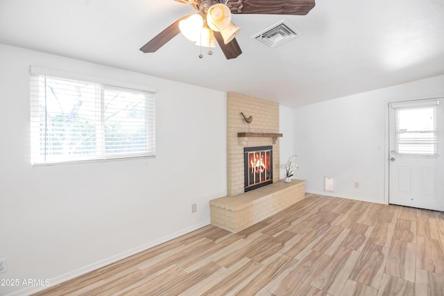 unfurnished living room with a brick fireplace, ceiling fan, and light wood-type flooring