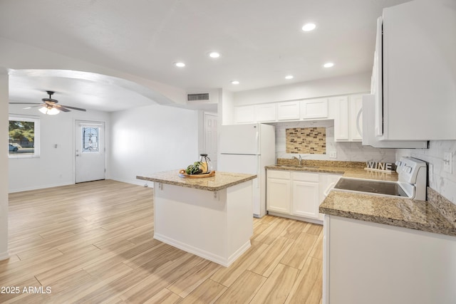 kitchen featuring backsplash, white cabinets, a center island, light stone counters, and white appliances