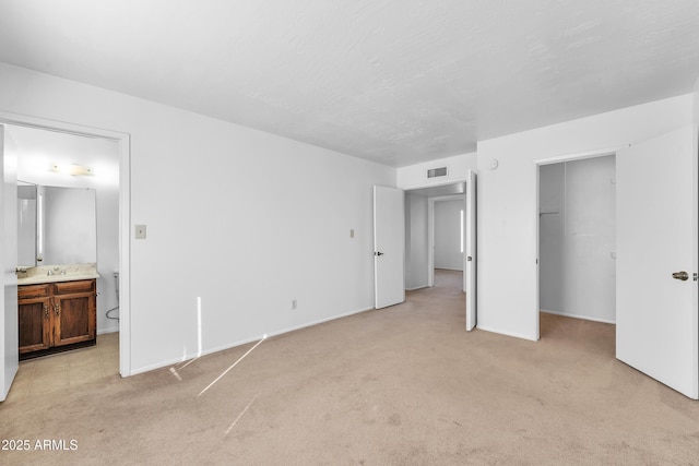 unfurnished bedroom with a spacious closet, ensuite bath, light colored carpet, and a closet