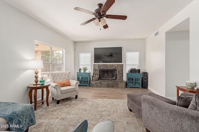 living room featuring a stone fireplace, light hardwood / wood-style flooring, and ceiling fan