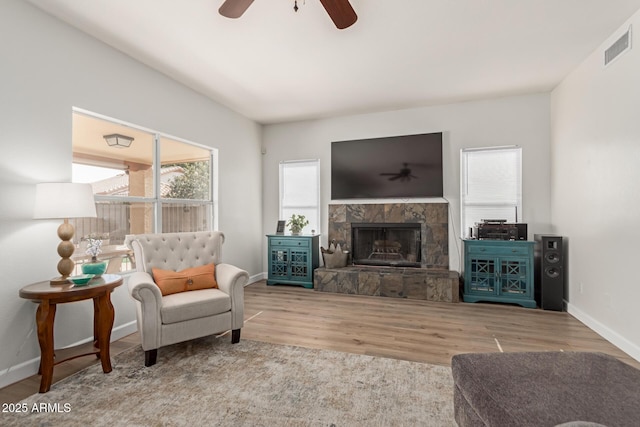 living room featuring a stone fireplace, hardwood / wood-style floors, and ceiling fan