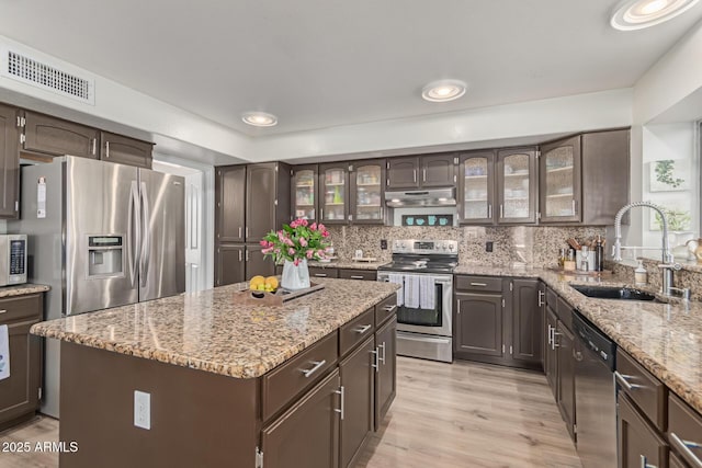 kitchen with sink, backsplash, stainless steel appliances, light stone countertops, and a kitchen island