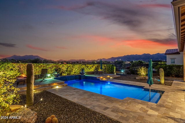 pool at dusk featuring a mountain view, a patio, and a hot tub