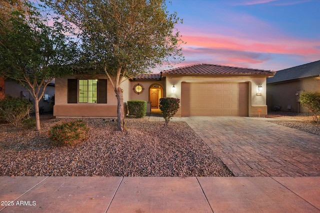 view of front of house with decorative driveway, an attached garage, a tile roof, and stucco siding