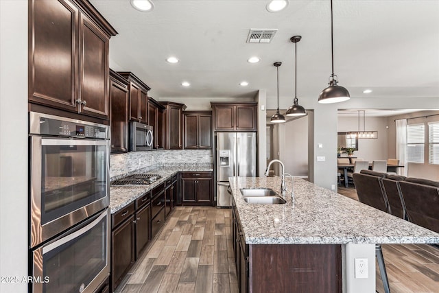 kitchen with dark brown cabinetry, visible vents, an island with sink, stainless steel appliances, and a sink