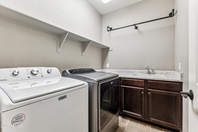 washroom featuring washing machine and clothes dryer, a sink, cabinet space, and wood tiled floor