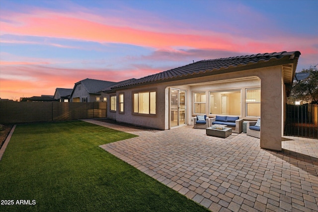 back of house at dusk featuring a patio, a fenced backyard, a yard, stucco siding, and an outdoor living space with a fire pit