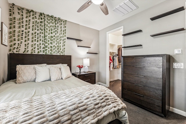 bedroom featuring a walk in closet, dark carpet, baseboards, and ceiling fan