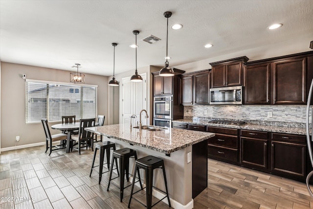 kitchen with visible vents, appliances with stainless steel finishes, decorative backsplash, wood tiled floor, and an island with sink