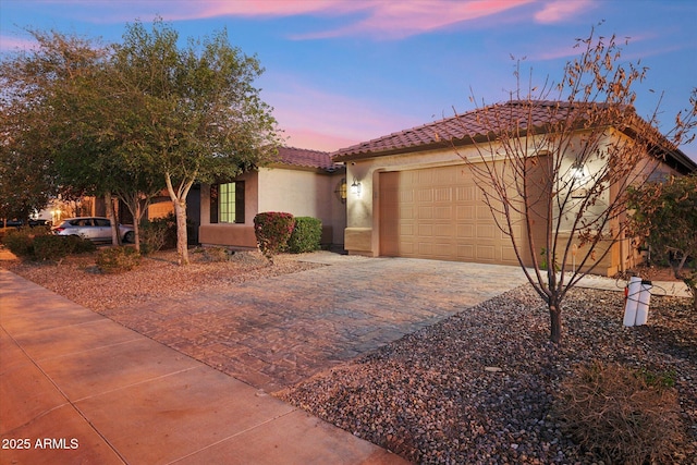 view of front of house with decorative driveway, an attached garage, a tile roof, and stucco siding