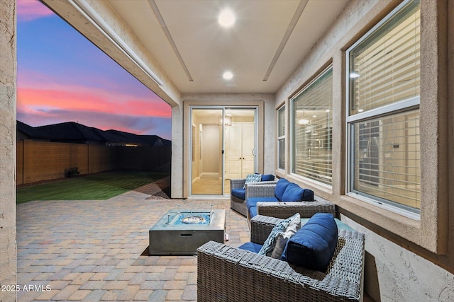 patio terrace at dusk featuring an outdoor living space with a fire pit and fence