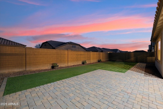 patio terrace at dusk with a fenced backyard and a lawn