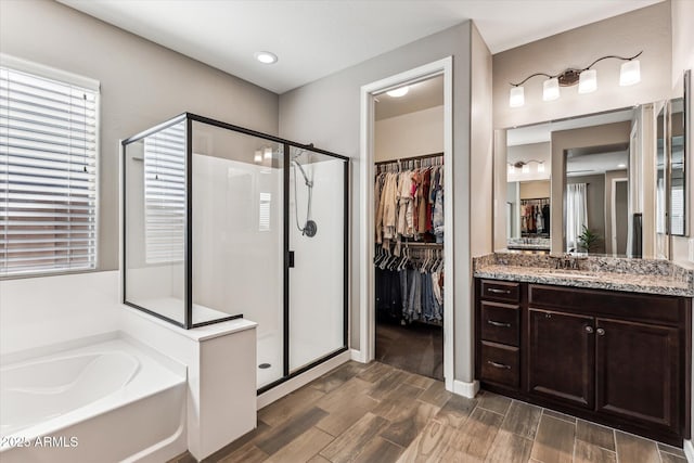 full bathroom featuring a stall shower, wood tiled floor, a bath, and vanity