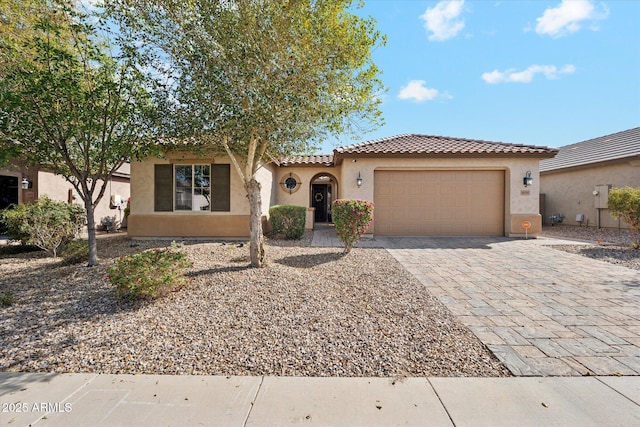 mediterranean / spanish-style home featuring a garage, decorative driveway, a tiled roof, and stucco siding