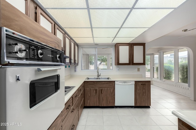 kitchen with white appliances, light tile patterned floors, a drop ceiling, a sink, and light countertops