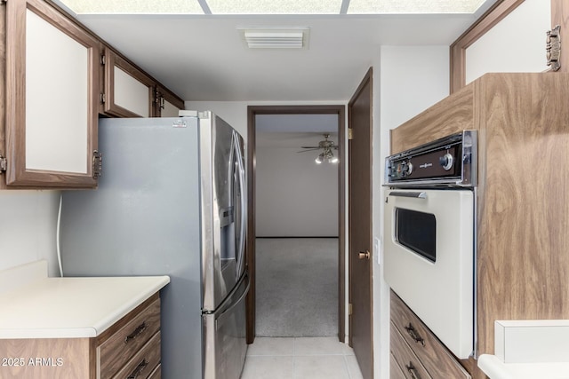 kitchen with oven, visible vents, stainless steel refrigerator with ice dispenser, light tile patterned flooring, and light countertops