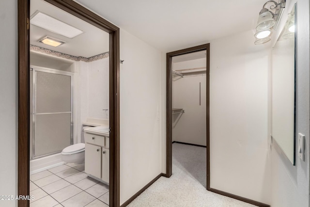 bathroom with vanity, baseboards, a spacious closet, an enclosed shower, and toilet