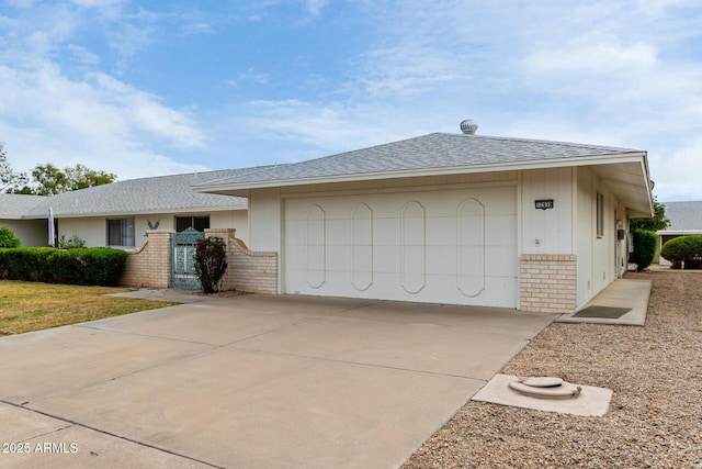 ranch-style home featuring a garage, brick siding, driveway, and roof with shingles