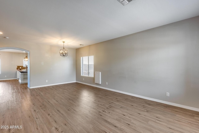 spare room with arched walkways, a notable chandelier, baseboards, and wood finished floors