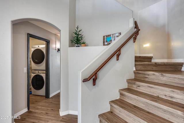 staircase featuring stacked washer / dryer, arched walkways, baseboards, and wood finished floors