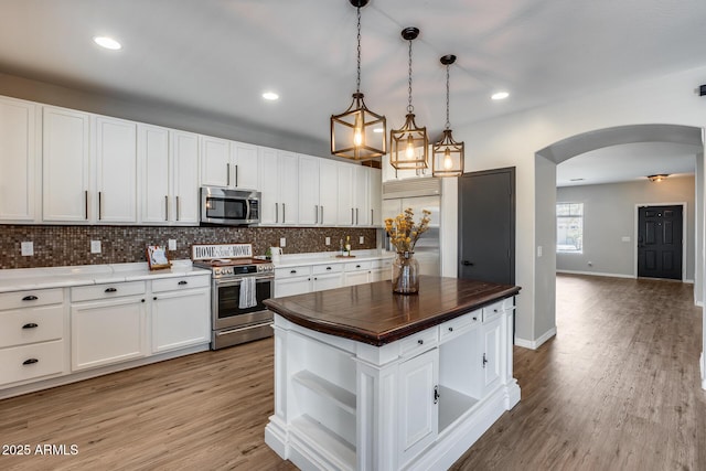 kitchen with arched walkways, white cabinets, appliances with stainless steel finishes, open shelves, and tasteful backsplash