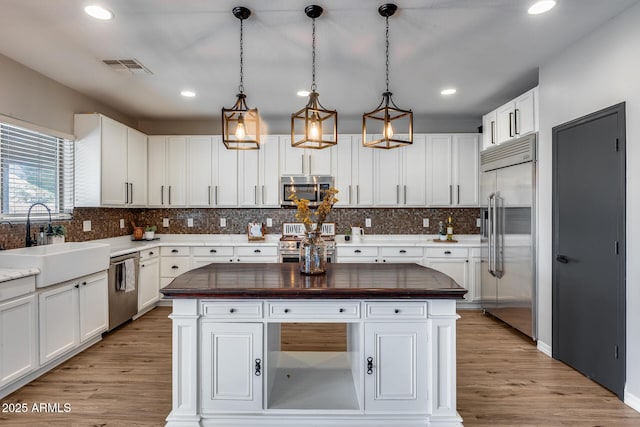 kitchen with a sink, visible vents, light wood-style floors, high quality appliances, and a center island