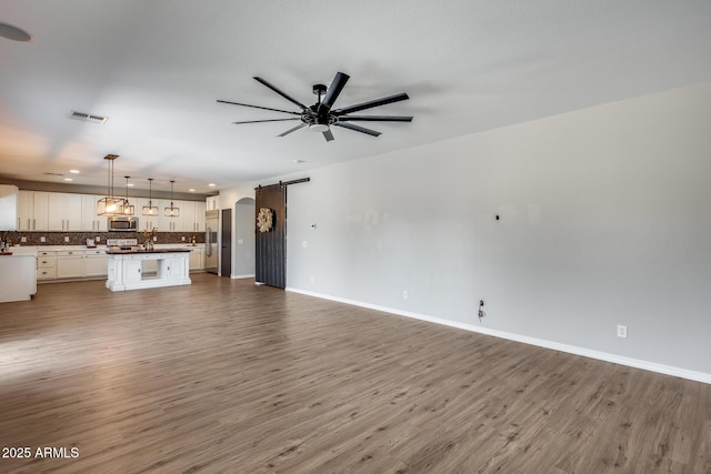 unfurnished living room with baseboards, a barn door, visible vents, and wood finished floors