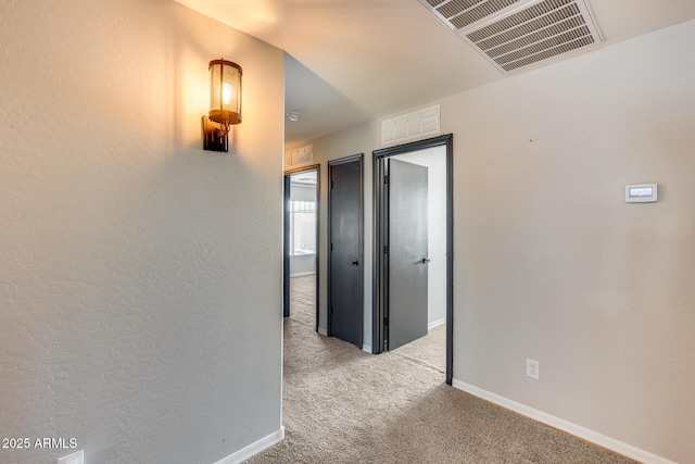 hall with carpet, visible vents, and baseboards