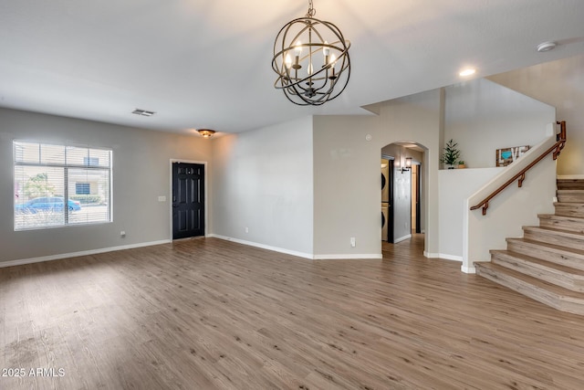 unfurnished living room featuring stairs, arched walkways, baseboards, and wood finished floors