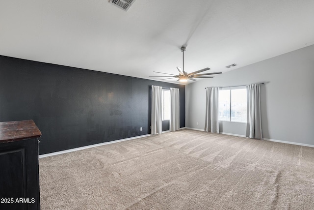 carpeted spare room featuring lofted ceiling, ceiling fan, an accent wall, visible vents, and baseboards