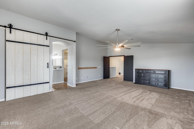 unfurnished living room with lofted ceiling, carpet, a barn door, and ceiling fan