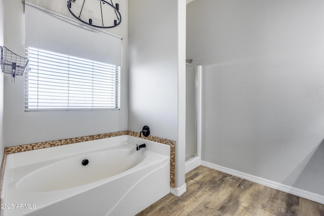 bathroom featuring wood finished floors, a shower stall, a bath, and baseboards