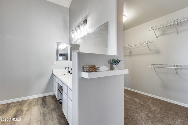 full bath featuring baseboards, a walk in closet, and vanity