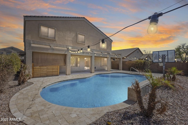 pool at dusk with a patio area, fence, and a fenced in pool