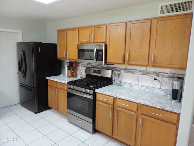 kitchen with decorative backsplash, light stone counters, visible vents, and stainless steel appliances