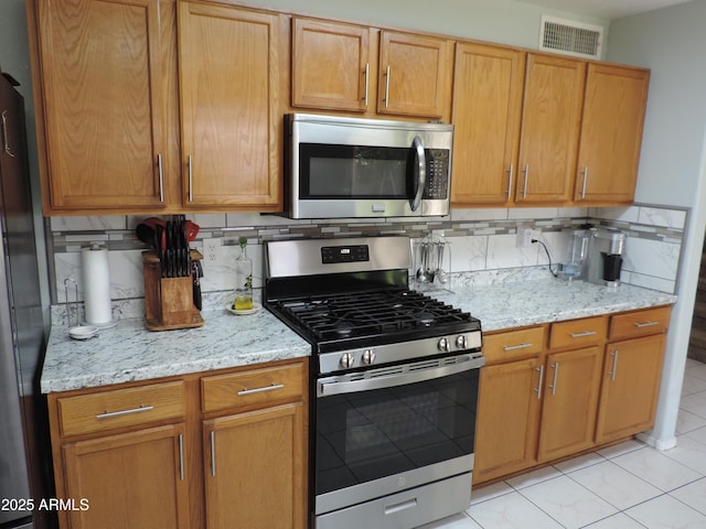 kitchen with tasteful backsplash, visible vents, stainless steel appliances, and light stone counters