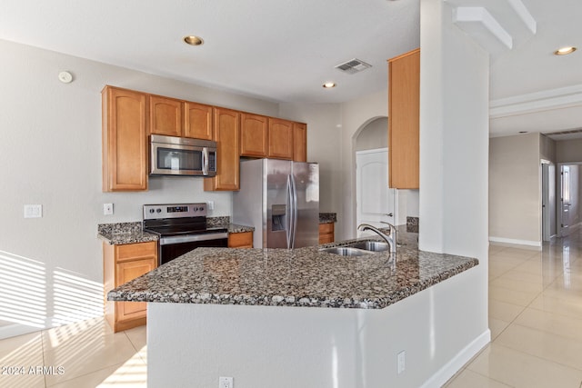 kitchen with sink, dark stone countertops, light tile patterned floors, appliances with stainless steel finishes, and kitchen peninsula