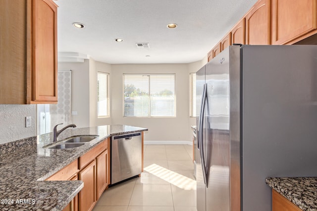 kitchen with light tile patterned floors, stainless steel appliances, dark stone countertops, and sink