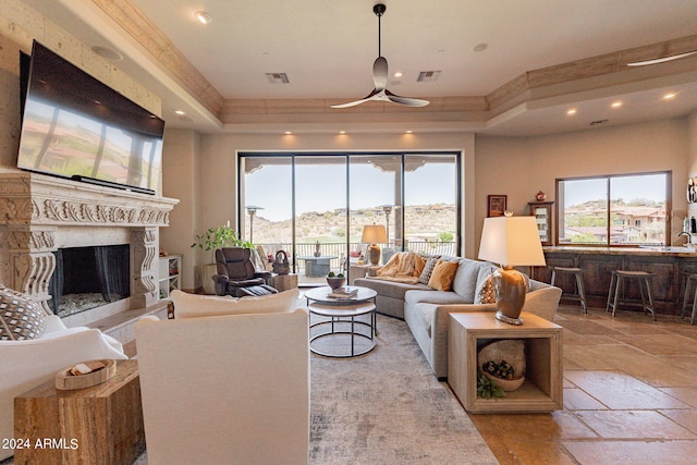 living room with a high end fireplace, ceiling fan, a raised ceiling, and sink