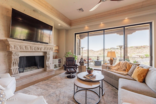 living room with a high end fireplace, ceiling fan, and a raised ceiling