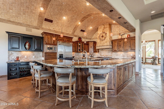 kitchen featuring premium range hood, built in appliances, backsplash, and a large island