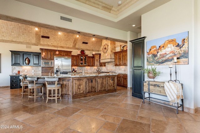 kitchen with a large island with sink, built in appliances, a kitchen bar, and tasteful backsplash