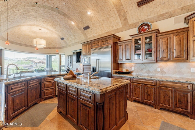 kitchen featuring vaulted ceiling, built in appliances, pendant lighting, a kitchen island with sink, and sink