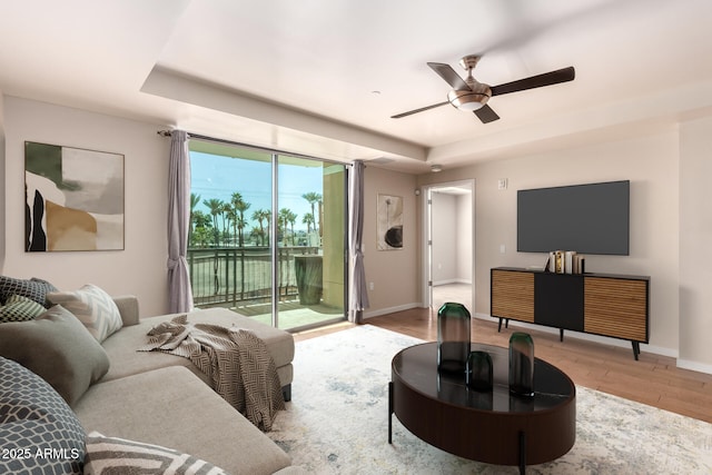 living room featuring a tray ceiling, light wood-type flooring, a ceiling fan, and baseboards