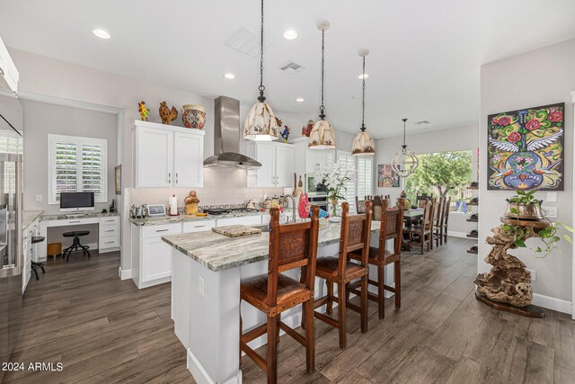 kitchen with white cabinets, an island with sink, decorative light fixtures, built in appliances, and dark hardwood / wood-style floors