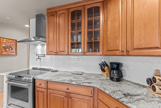 kitchen with stainless steel electric stove, backsplash, light stone countertops, and wall chimney exhaust hood