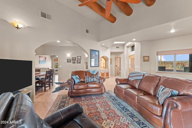 living room featuring beamed ceiling, a towering ceiling, light wood-type flooring, and ceiling fan